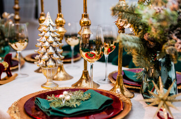 New Year table setting. The table is decorated with golden plates, candles and candlesticks, glasses and Christmas tree branches