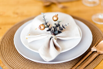 New Year table decor. A white napkin with decor lies on the plate, under the plate there is a bronze-colored countertop