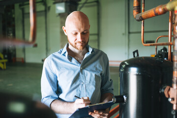 Adult bald smiling attractive man forty years with beard in blue shirt businessman. Engineer near the control cabinet of refrigeration equipment in warehouse