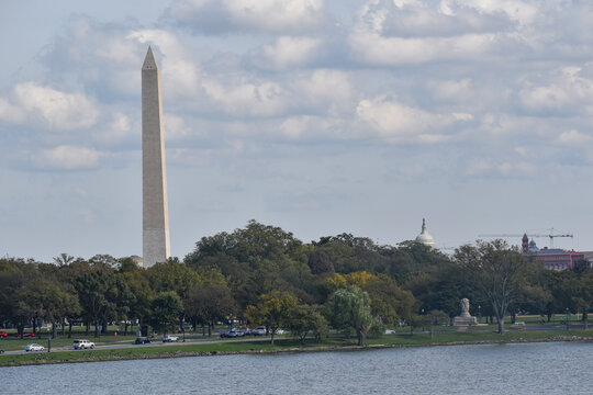 Washington, DC, USA - October 25, 2021: The Washington Monument and the Top of the Rotunda of the U.S. Capitol Peak Over the Tree Line as Seen from Across the Potomac River