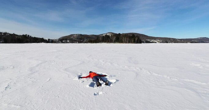 Girl making snow angel on frozen lake having fun in winter wonderland nature landscape, Young woman doing snowangel