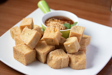 Fried tofu with Thai sweet dipping sauce in a white plate on the wooden floor