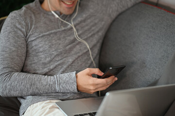 Cropped shot smiling man using smart phone and laptop computer on sofa.