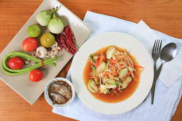 Green papaya salad with pickled fish on white plate against wooden table background.