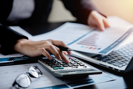 Close up of Businesswomen or Accountant using a calculator and laptop computer with analytic business report graph and finance chart at the workplace, financial and investment concept.