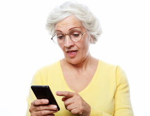 Pretty senior female in casual outfit using modern smartphone and laughing out loud while standing on white background. Old woman watching funny videos on internet.