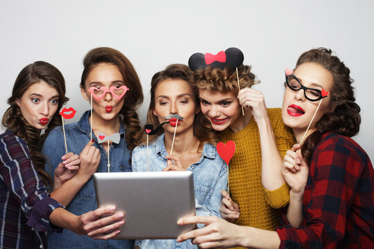 five hipster girls friends holding party props and taking selfie with digital tablet, studio shot over gray background
