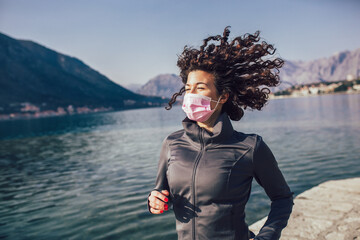 Running woman. Female runner jogging with protective mask during outdoor workout on beach.