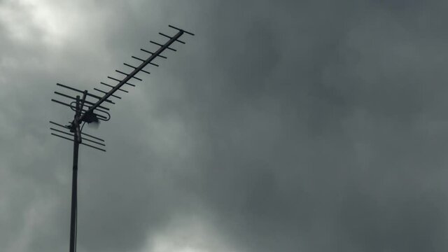 Close-up of a television antenna against a background of dark gray rain clouds. Timelapse