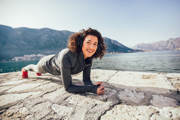 Athletic young woman with curly hair doing exercises on the beach