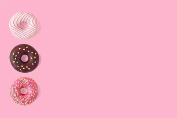 three delicious sweet donuts with sprinkles lie on a blue background, bright donut on a pink background