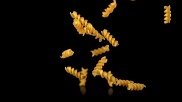 Super slow motion dry fusilli pasta falls on the table. On a black background. Filmed on a high-speed camera at 1000 fps. High quality FullHD footage