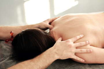 A male masseur conducts spa treatments for a young woman who is lying face down on a couch.