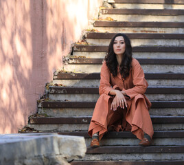 Fashion model in brown coat sitting on stairs outdoor