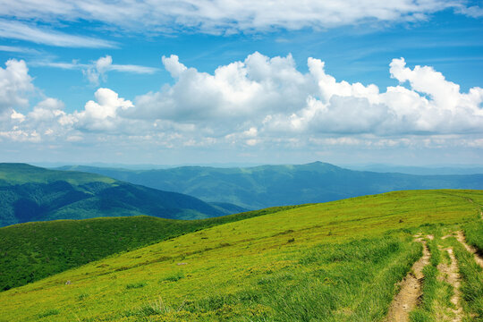 country road through alpine meadow of carpathian mountain. beautiful nature landscape in summer. scenery with open view in to the distant ridge and valley. wonderful sky with clouds above the horizon
