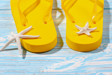 yellow rubber beach flip flops and starfish on a blue wooden background, place under the text