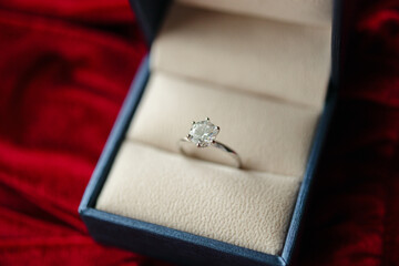 Diamond ring in jewelry gift box on red fabric background