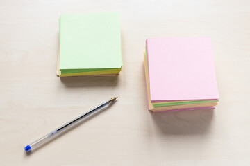 top view of stacks of blank colorful sheets of memo paper and simple blue pen on light brown wooden board