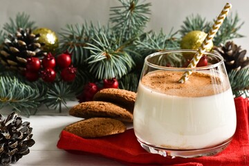 Two glass homemade winter eggnog with cinnamon, and fir tree branches, cookies, red napkin on white wooden table. Traditional Christmas dessert