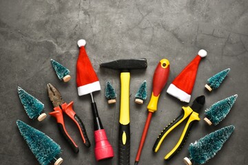 Christmas construction tools. Hammer, screwdrivers, brushes, pliers with decorative Christmas trees, santa claus hats on a gray background. Advertising concept. Card. Copy space, flat lay.
