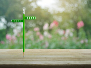 2022 and 2021 direction sign plate with green pencil on wooden table over blur pink flower and tree in garden, Business happy new year 2022 planning cover concept