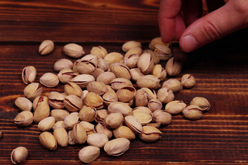 fingers take pistachio nuts scattered on a wooden table