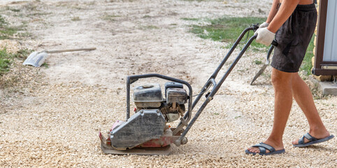 A worker lays down gravel and sand for paving slabs.