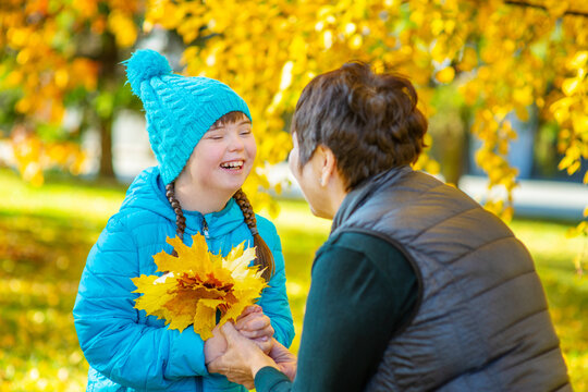 A girl with down syndrome with her mother outdoors in an autumn park collecting a bouquet of fallen leaves
