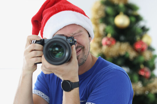 Man in red santa hat taking pictures with camera near christmas tree