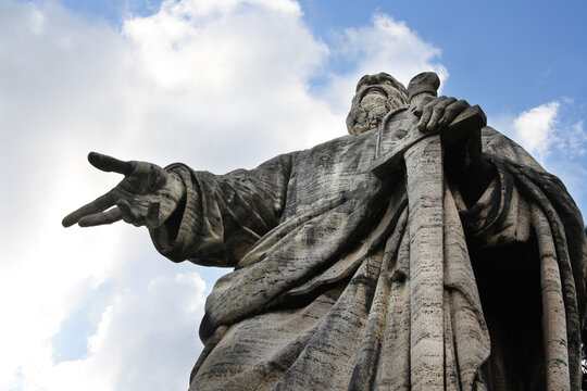 The Apostle Paul with his sword drawn in his hand. Old giant statue in front of the Basilica of Saints Peter and Paul in EUR district, Rome. Low angle view on cloudy sky.