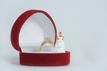 Women miniature people fitting wedding dress standing above ring box, isolated white background