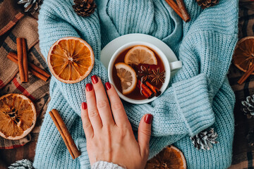 Blue sweater and cup of hot tea with lemon cinnamon sticks and anise star. Dry slices of citrus...