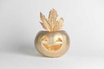 Carved scary smiling pumpkin painted in gold color with leaves on a grey background. The concept of Halloween decorations.