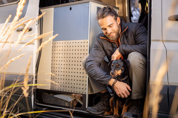 Man and his pet dog sitting in the doorway of a camper van - obrazy, fototapety, plakaty