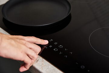 Modern kitchen appliance. Woman hand turn on induction stove to cook. Finger touching sensor button...