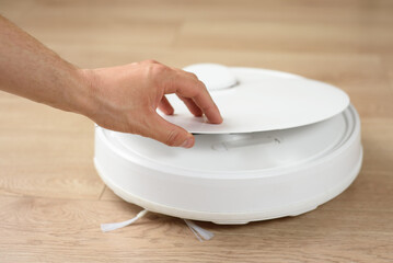 male hand opens the lid of the robot vacuum cleaner for cleaning or replacing the filter