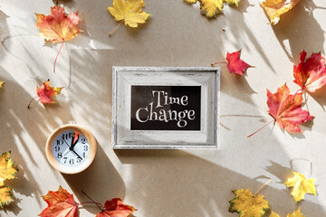 Time change in Autumn. Wooden alarm clock with one hour mark with dry Fall leaves on recycled...