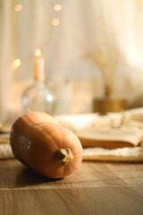 Butternut squash, soft blanket, open book, reading glasses and lit candles. Autumn season, hygge at home. Selective focus.