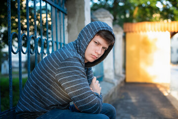 Young introvert teenage student on a solo walk in the park in summer wearing a hoodie with a...
