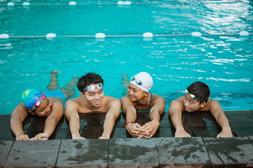 four asian teenagers in swimsuits chatting while resting by standing by the pool