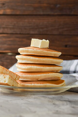 a stack of pancakes with a piece of butter on a wooden background. front view