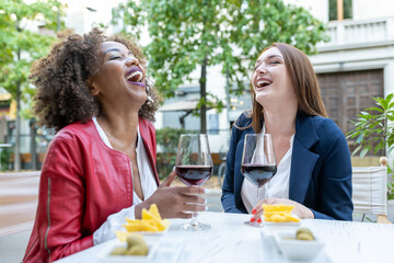 Two happy female friends laughing and toasting with red wine, adult people enjoying a break from work, colleagues gathering after a hard work day, women celebrating something
