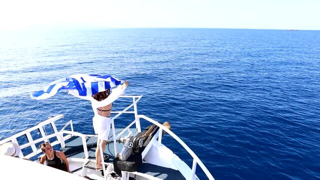 Lefkada, Greece - September 04, 2021: woman holding greece flag sail on the boat bend around lefkada island