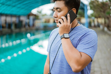 a swimming coach wearing a stopwatch makes a phone call using a mobile phone