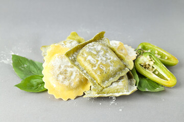 Raw ravioli with spices on light gray background