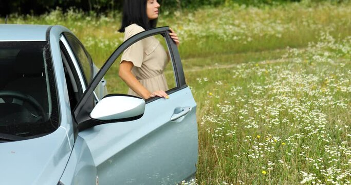 Woman gets out of the car ooking around and walking on the flowers field, meadow in countryside during journey, travel, feel the nature, alone trip, relax.