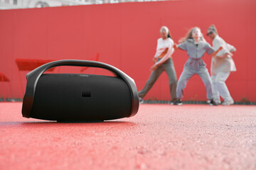 Wireless outdoor portable speaker playing music on dance floor on red background with dancing girls. Product placement