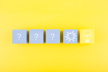 Creativity, brainstorming and fresh ideas concept. Light bulb and question signs drawn on toy cubes on yellow background