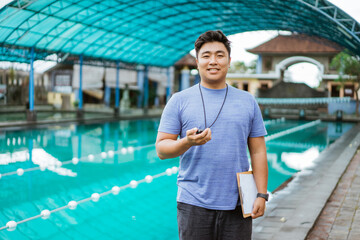 smiling coach holding clipboard and stopwatch while standing