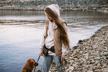 young woman and dog retriever walks on river shore at autumn season